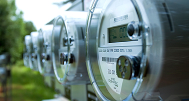 Close-up of several AMI electricity meters with digital readouts mounted on a utility panel.