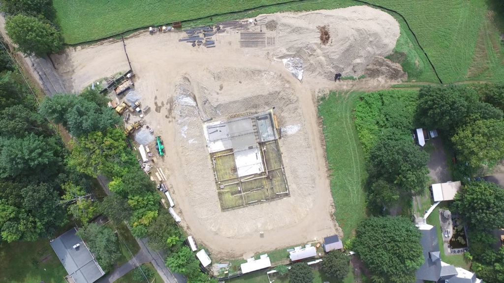 An aerial view of the Whitcomb Avenue Water Treatment Facility construction site, showing the building foundation under development and surrounding equipment.